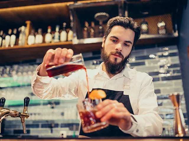 Ein Bartender kippt einen Drink in einen Tumbler